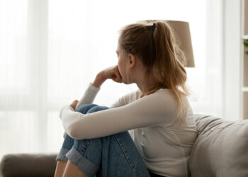 Side view young woman looking away at window sitting on couch at home. Frustrated confused female feels unhappy problem in personal life quarrel break up with boyfriend or unexpected pregnancy concept