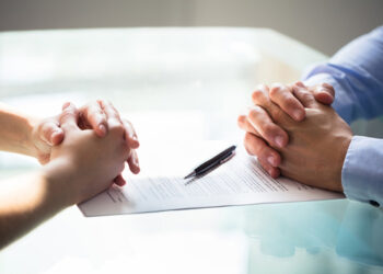 Close-up Of Two Businesspeople Hand With Document On Desk