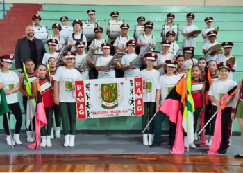 Crianças da Fanfarra Maria Gai, uniformizadas, tocando instrumentos de percussão e melódicos em apresentação de concurso em Curitiba.
