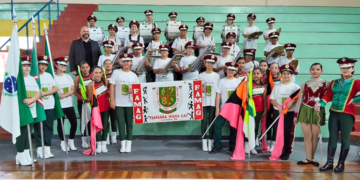 Crianças da Fanfarra Maria Gai, uniformizadas, tocando instrumentos de percussão e melódicos em apresentação de concurso em Curitiba.