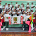 Crianças da Fanfarra Maria Gai, uniformizadas, tocando instrumentos de percussão e melódicos em apresentação de concurso em Curitiba.
