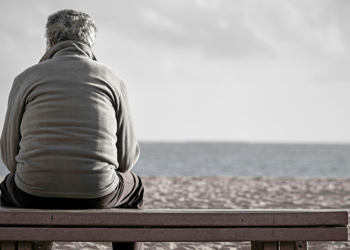 Homem sentado sozinho em um banco de parque ou praça, olhando o vazio, ilustrando o sentimento de luto por possibilidades e a dor da solidão.