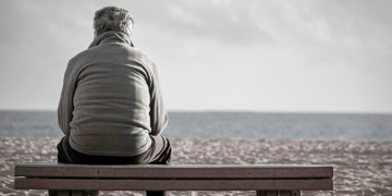 Homem sentado sozinho em um banco de parque ou praça, olhando o vazio, ilustrando o sentimento de luto por possibilidades e a dor da solidão.