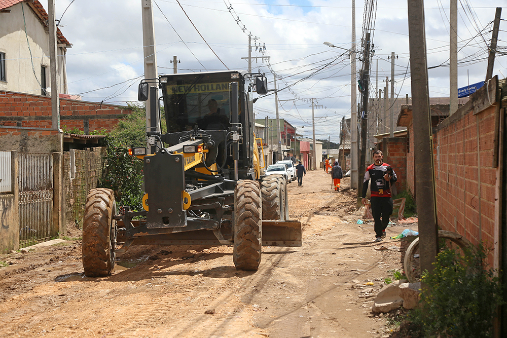 Obras de escavação e pavimentação em uma das ruas do Bairro Caximba, em Curitiba, mostrando a implantação de nova drenagem, asfalto e calçadas.