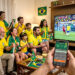 Pessoa segurando um smartphone na sala de casa exibindo gráficos e propagandas de apostas esportivas de futebol na tela.