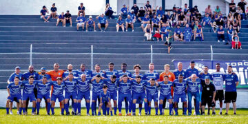 Equipe do Urano posa no gramado com uniformes azuis na estreia da Taça Paraná 2026, com torcedores na arquibancada ao fundo