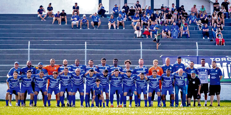 Equipe do Urano posa no gramado com uniformes azuis na estreia da Taça Paraná 2026, com torcedores na arquibancada ao fundo