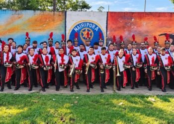 Integrantes da Banda Musical do Caximba uniformizados e com instrumentos diante de um mural em Mairiporã.