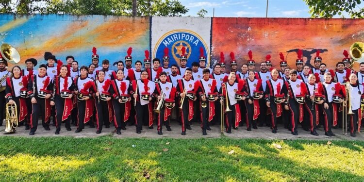 Integrantes da Banda Musical do Caximba uniformizados e com instrumentos diante de um mural em Mairiporã.