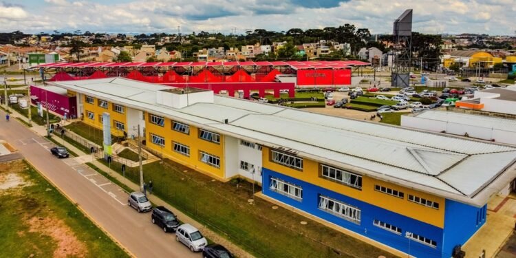 Vista aérea da Rua da Cidadania do Tatuquara, com prédios coloridos e veículos estacionados ao redor.