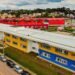 Vista aérea da Rua da Cidadania do Tatuquara, com prédios coloridos e veículos estacionados ao redor.