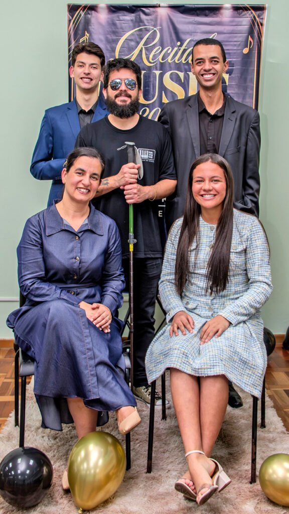 Grupo posa diante do painel do recital de música da Escola Partituras.