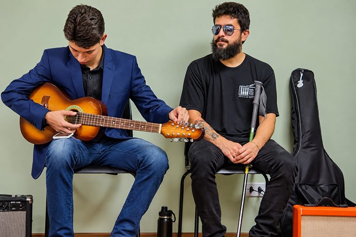 Músico ajusta instrumento de cordas ao lado de outro participante do recital.